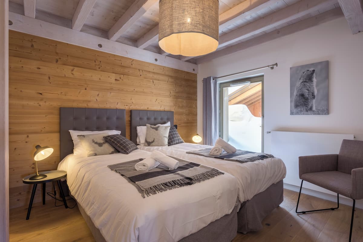 Une chambre avec un grand lit, deux tables de chevet, une chaise, un luminaire suspendu et une fenêtre donnant sur un beau paysage.
