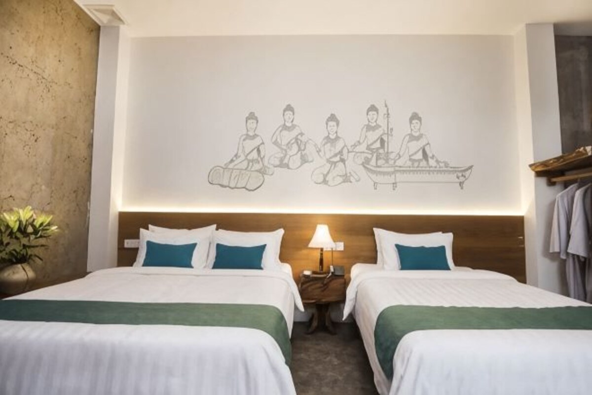 Une chambre d’hôtel avec deux lits, une œuvre d’art accrochée au mur, une lampe de chevet et une petite table.
