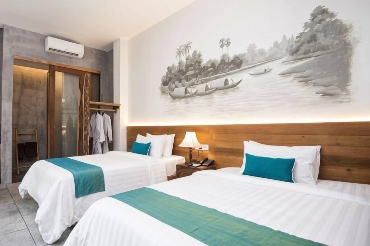 Une chambre d’hôtel avec deux lits, une tête de lit en bois, une table de chevet avec une lampe, une armoire et un climatiseur fixé au mur.