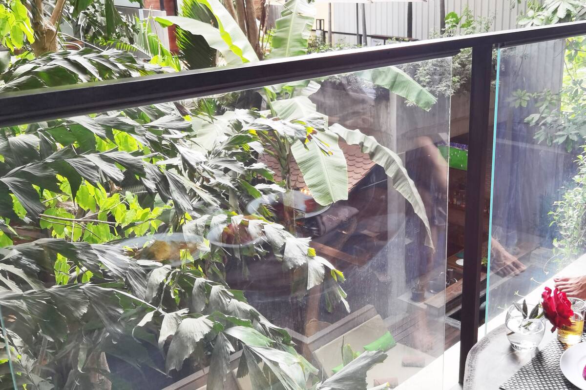 Une personne assise à une table, devant un ordinateur portable, entourée de verdure et avec un repas à portée de main.