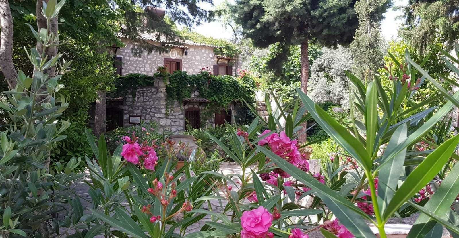 A stone building with a rustic facade, surrounded by lush greenery and flowering plants.