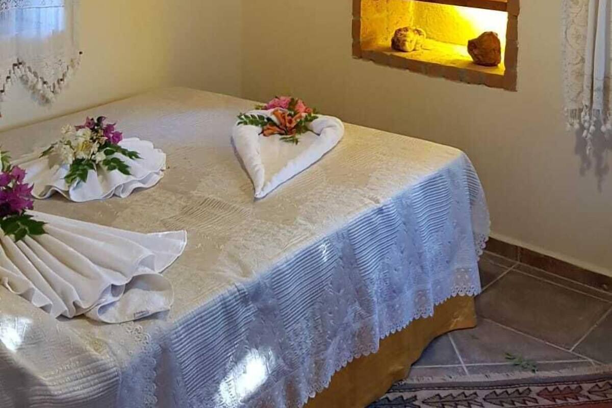 Un dormitorio con techo de madera, cama con cubrecama blanco, espejo en un nicho de arco y ventana con cortinas.