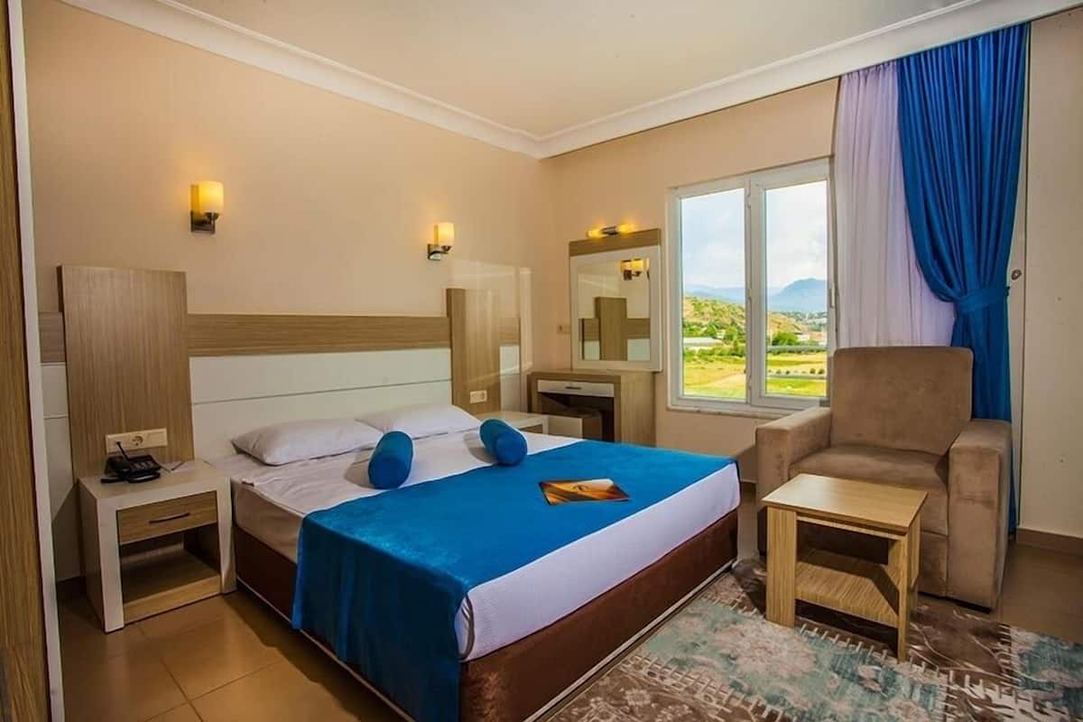 A hotel room with a bed, a chair, a desk, and a window with a view of the outdoors.