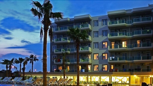 A hotel with multiple balconies, a pool area with sun loungers, and a well-lit outdoor dining area. - Grand Akca Hotel (Gazipasa)