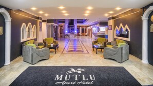 A hotel lobby with a central reception desk, two sofas, a carpet with the hotel name, and a geometric patterned floor. - Mutlu Apart Otel (Didim)