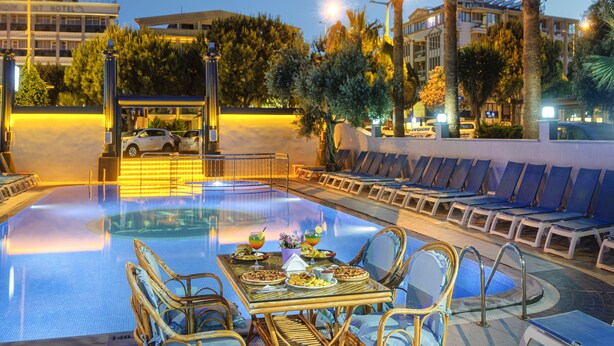 A poolside dining area with a table set for two, lounge chairs, and a pool. - Mutlu Apart Otel (Didim)