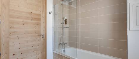 Een badkamer met een houten deur, een glazen douchecabine en beige betegelde wanden.