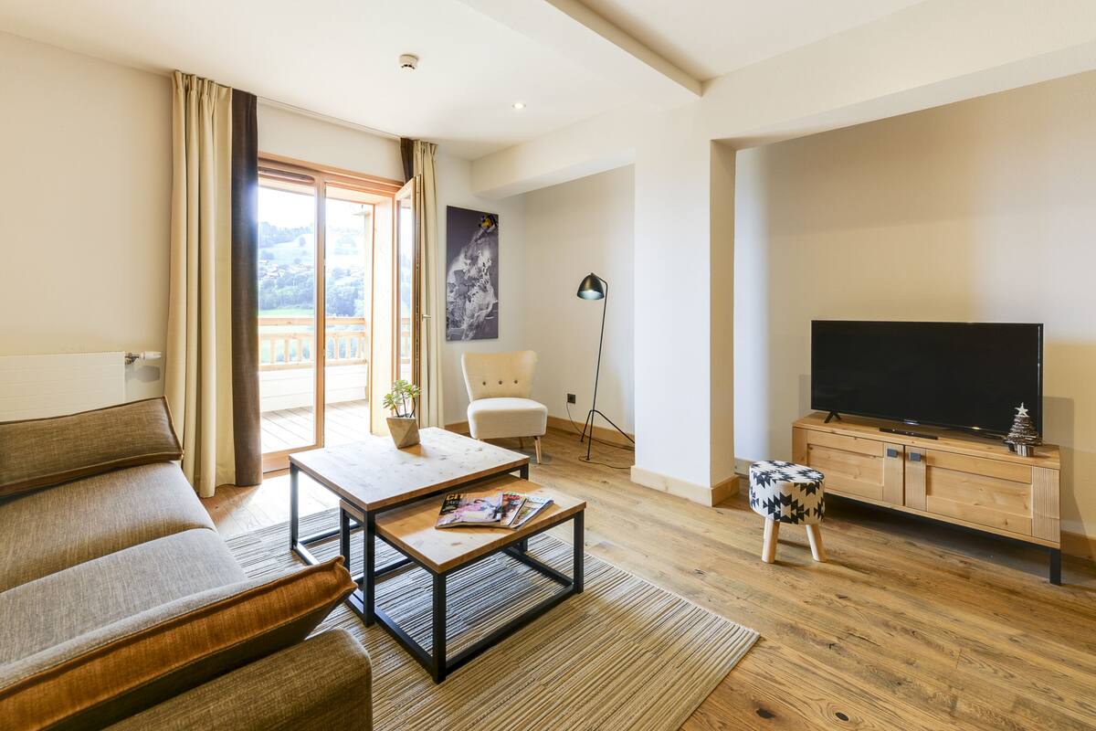 Un salon moderne avec un canapé, une table basse, un téléviseur et un balcon agrémenté de rideaux.