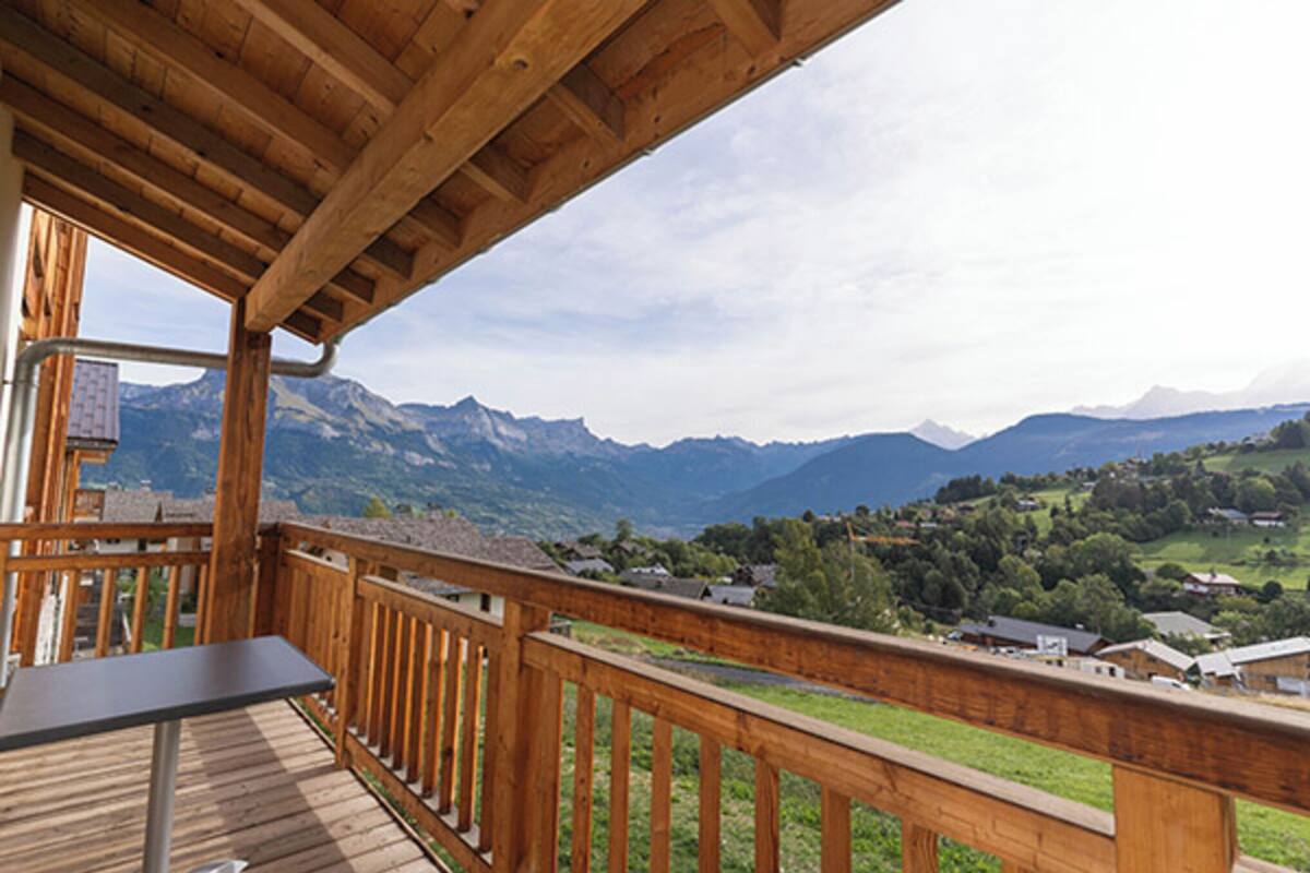 Une terrasse en bois avec une table, offrant une vue sur un paysage montagneux parsemé de maisons.