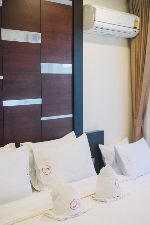 A hotel room with a wooden headboard, white bedding, and an air conditioning unit.