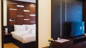 A modern hotel room with a neatly made bed, a flat-screen TV on a wooden stand, and a small table with a vase of flowers. - Luxury Residence (Chiang Mai)