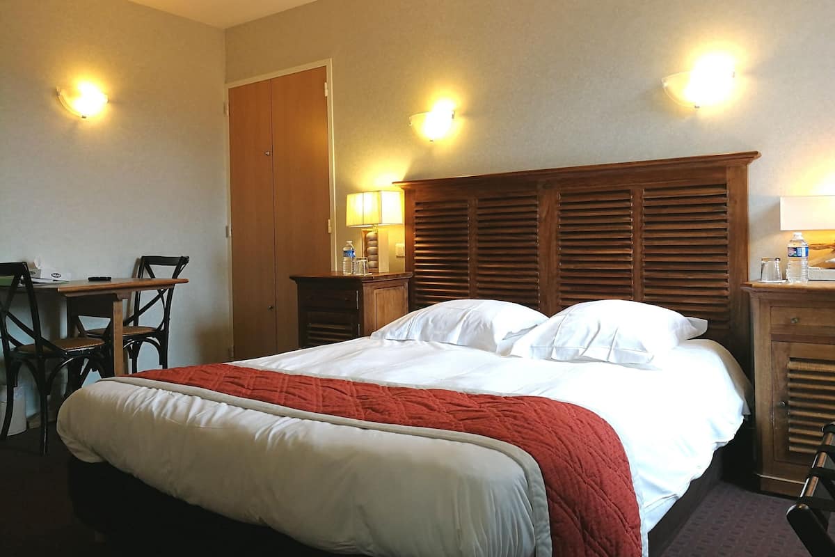 Een hotelkamer met een bed, een bureau met stoel, een houten garderobe en twee wandlampen.