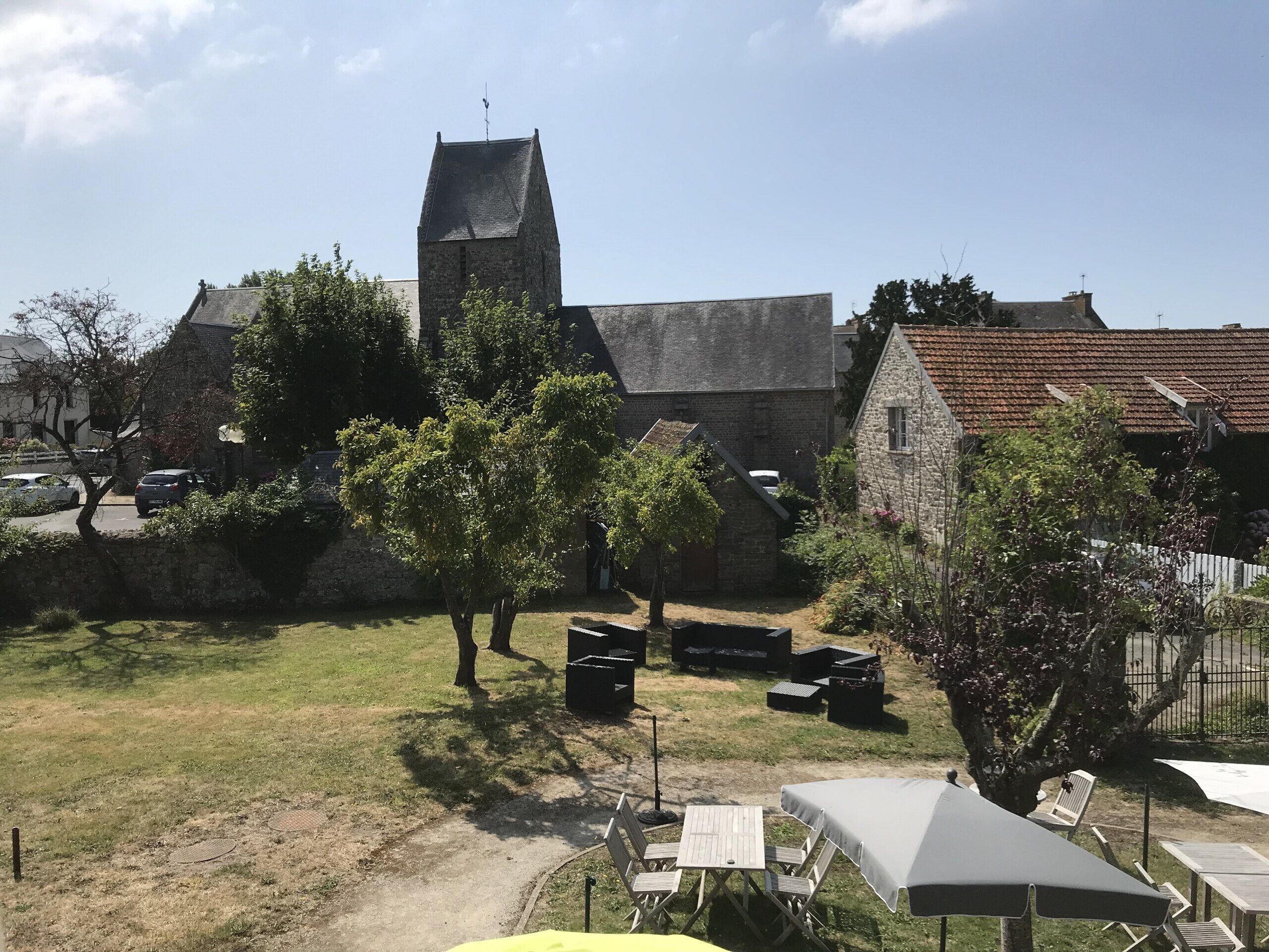 A courtyard with stone buildings, a church tower, and outdoor seating.