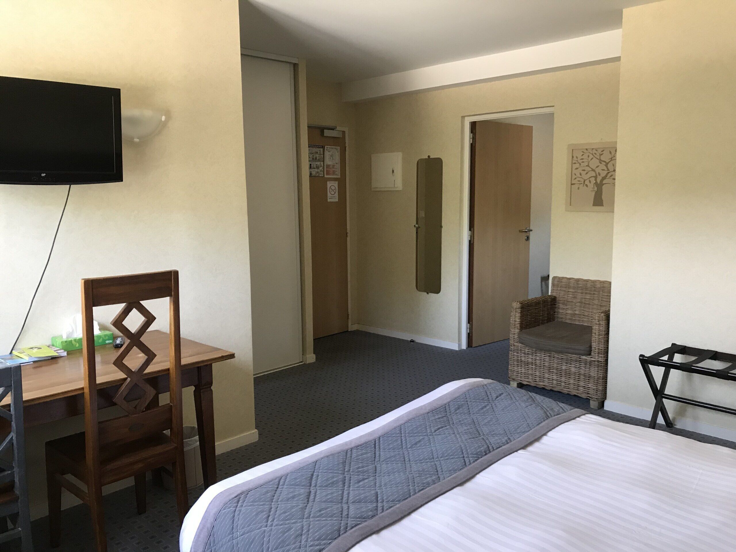A hotel room with a bed, a desk, a chair, a television, and a door leading to another room.