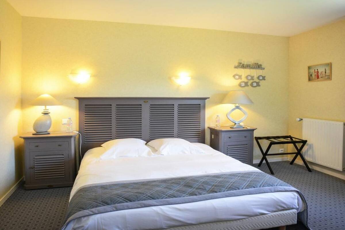 Een hotelkamer met een bed, twee nachtkastjes met lampen, een radiator en een wanddecoratie.