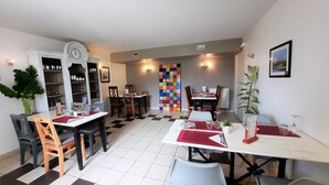 A dining area with checkered flooring, multiple tables with chairs, a clock, and a colorful wall decoration.