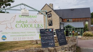 A restaurant sign for Auberge de Caroles with a stone wall, a wooden building, and a green awning.