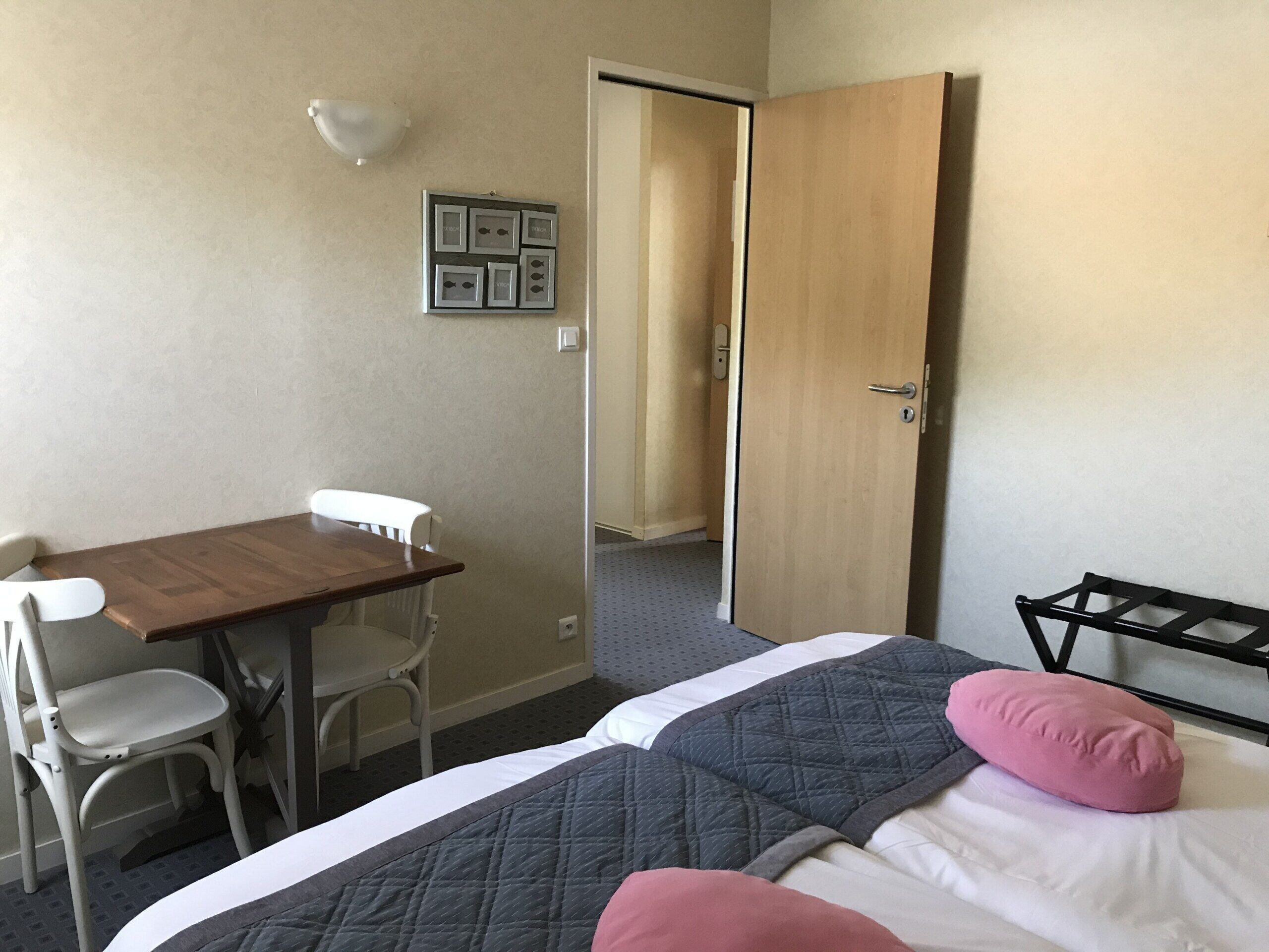 A hotel room with a wooden desk, two white chairs, a bed with a quilted cover, and a wall-mounted light fixture.