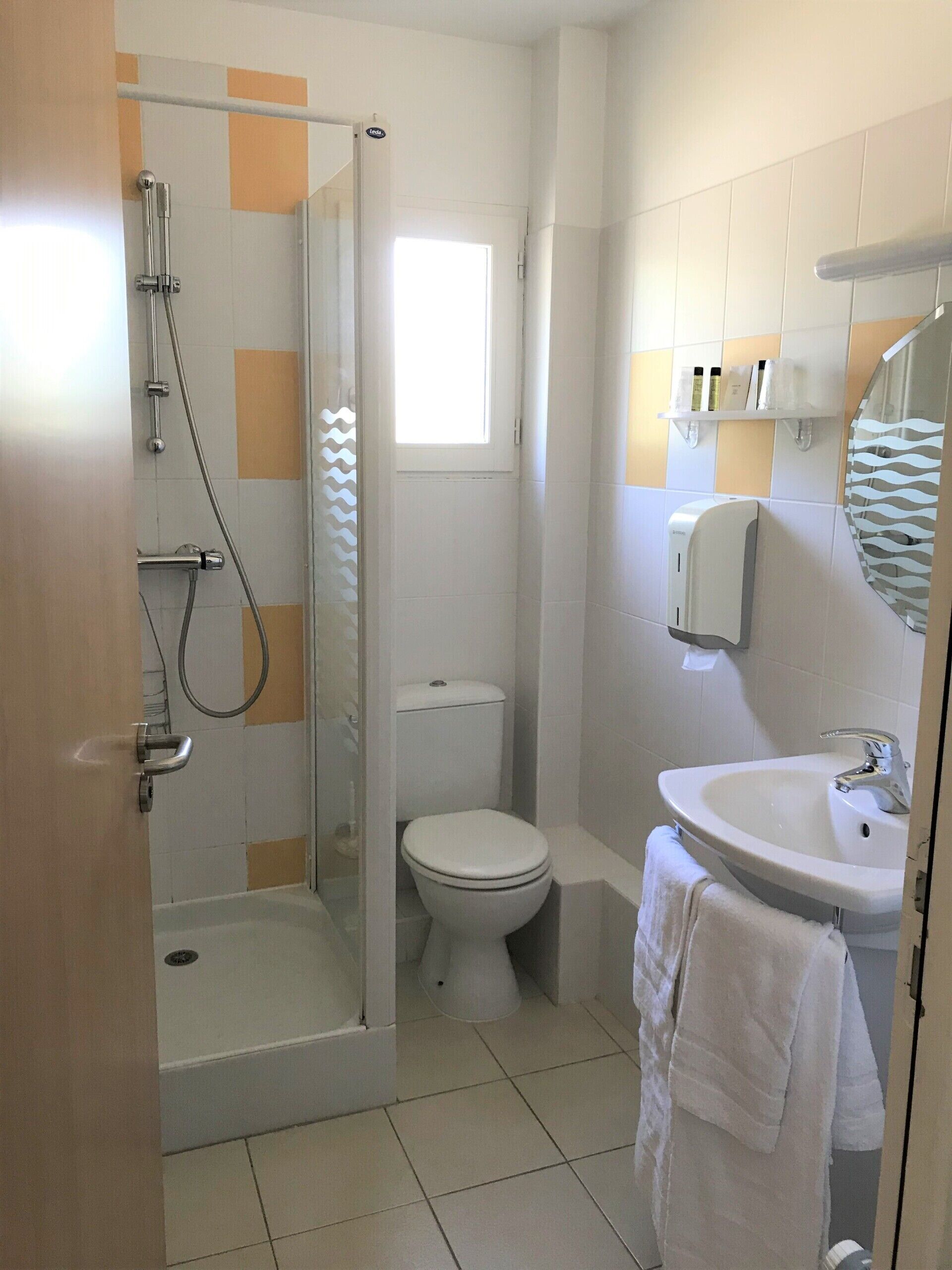 A bathroom with a glass-enclosed shower, a toilet, and a sink with a towel hanging nearby.