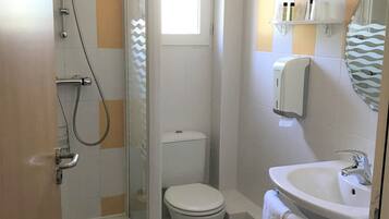 A bathroom with a glass-enclosed shower, a toilet, and a sink with a towel hanging nearby.