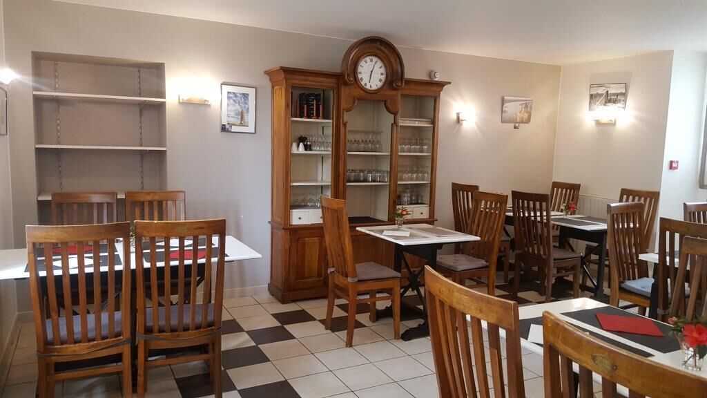 Un comedor con sillas y mesas de madera, un mueble de madera grande con cristalería, y un reloj de pared.