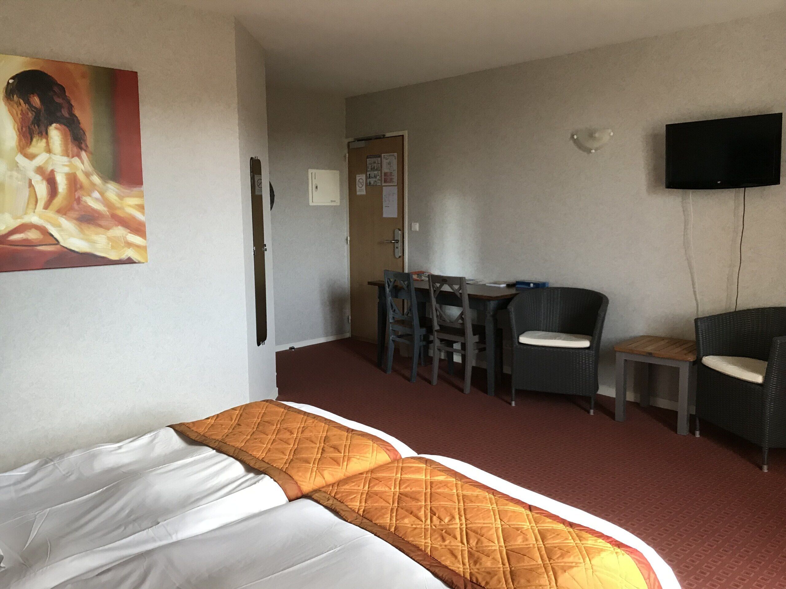 Una habitación de hotel con cama, escritorio, dos sillas, televisión y un cuadro en la pared.