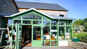 A green glass-fronted building with a wooden interior, a stone wall on one side, and a metal roof.
