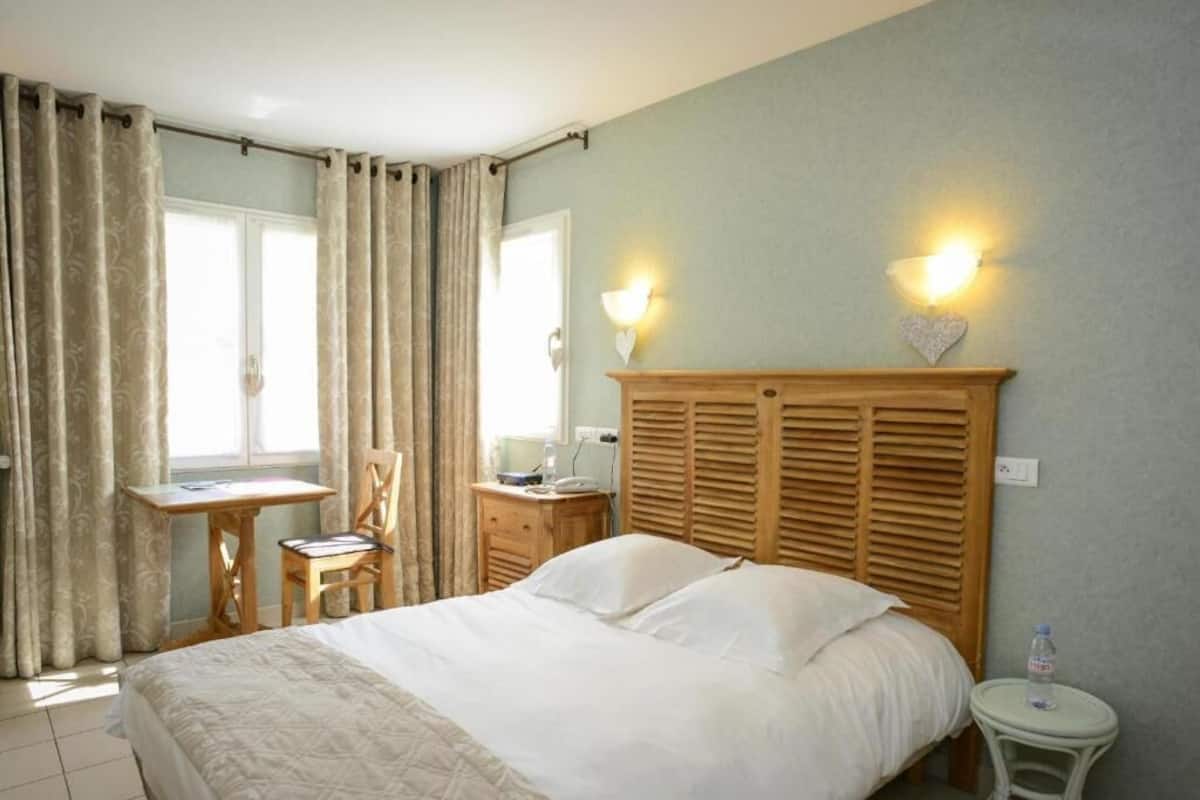 Hotelkamer met een groot bed, een houten hoofdbord, een bureau met stoel en twee wandlampen.