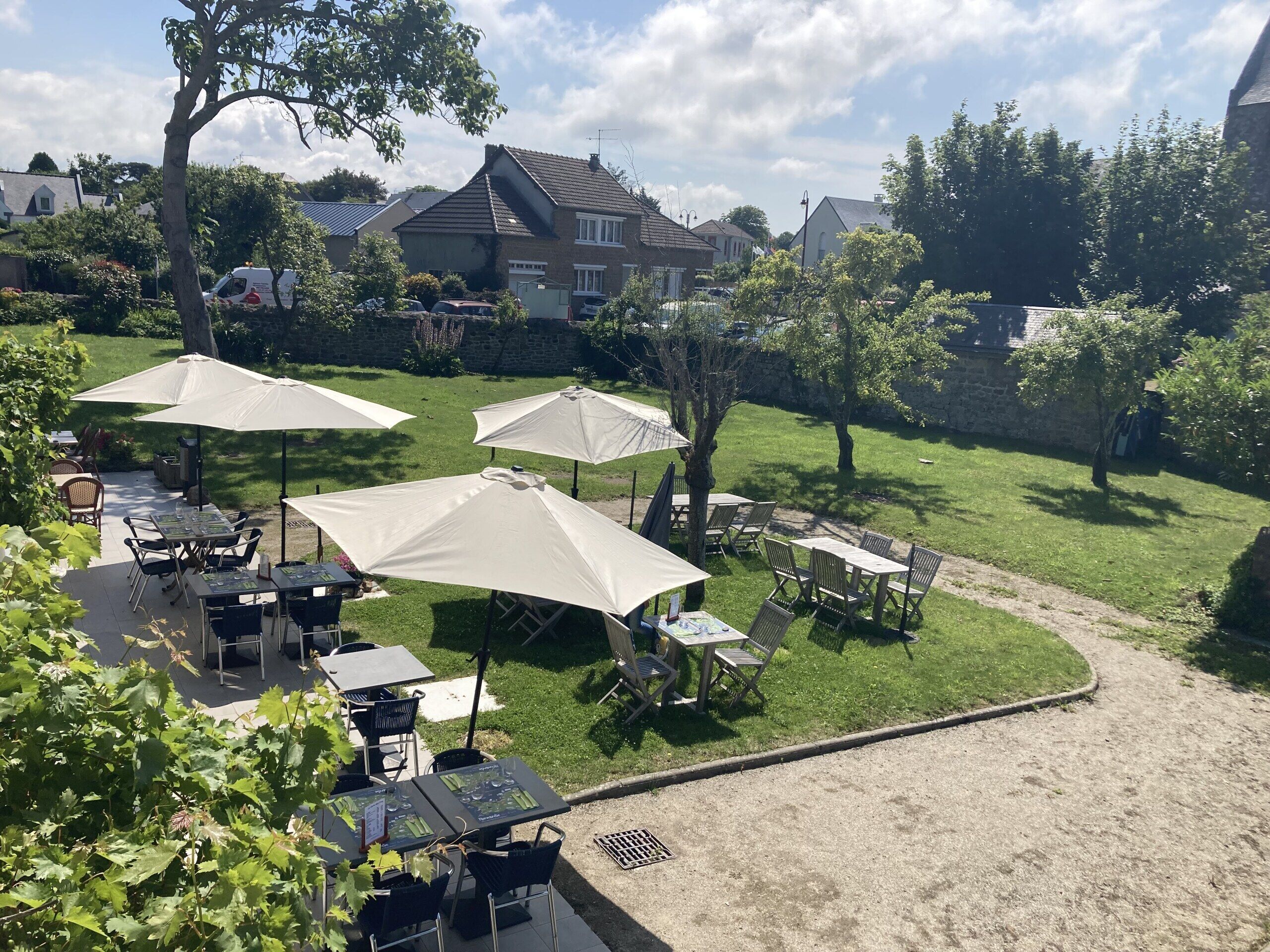 Een terras met tafels en stoelen, omgeven door een gazon en bomen.