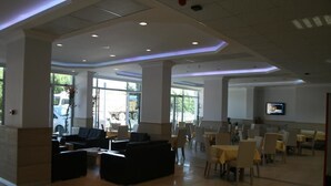 A spacious indoor area with seating arrangements, large windows, and a flat-screen TV on the wall. - Hotel Kale Palace (Gökçeada)