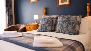A neatly made bed with a plaid bedspread, two pillows with floral patterns, a bedside lamp, and a wooden nightstand. - The Greyhound Inn & Hotel (Usk)