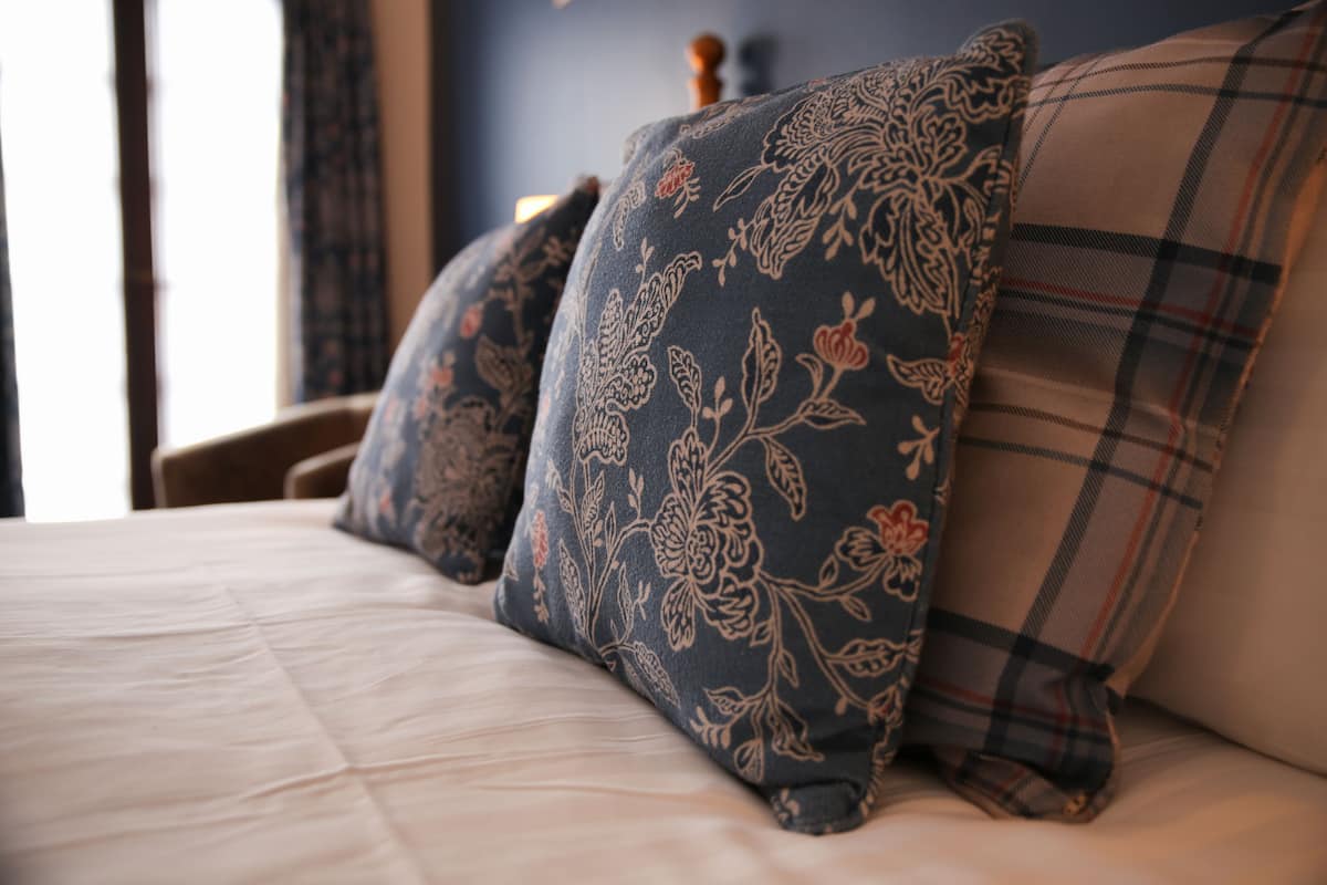 A bed with floral and plaid pillows, a wooden headboard, and a window with curtains.
