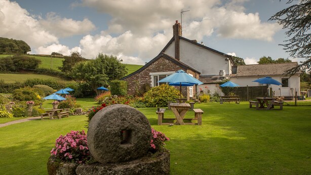 A stone house with a white exterior, surrounded by a well-maintained lawn and several outdoor tables and benches. - The Greyhound Inn & Hotel (Usk)