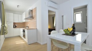 A modern kitchen with white cabinets, a wooden countertop, and a dining area with a white table and chairs. - Apartments Corte (Privlaka)