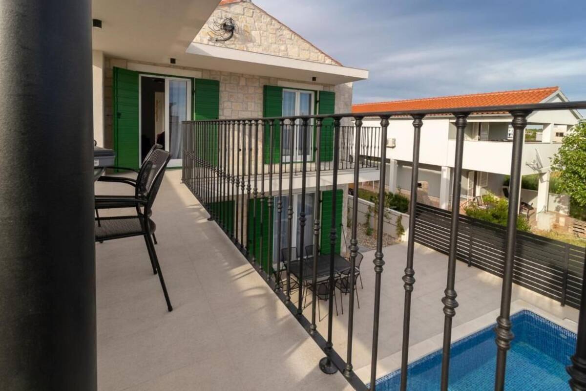 Ein Balkon mit Pool, grünen Fensterläden und Gartenmöbeln.
