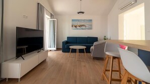A modern living room with a flat-screen TV, a blue sofa, a small round table, and wooden bar stools. - Apartments Corte (Privlaka)