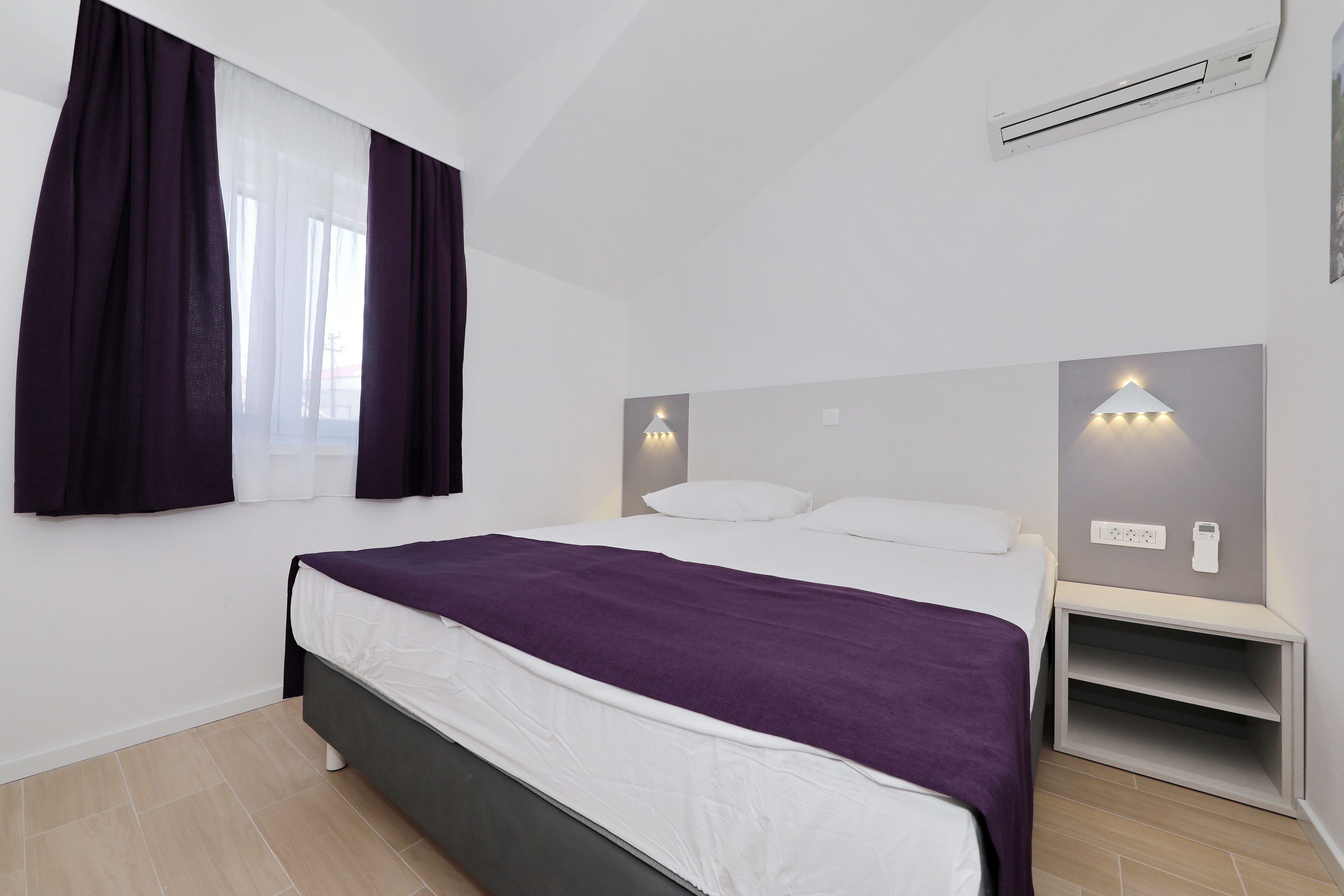 Ein modernes Schlafzimmer mit einem Bett, weißen Vorhängen und einem Nachttisch mit Lampe.