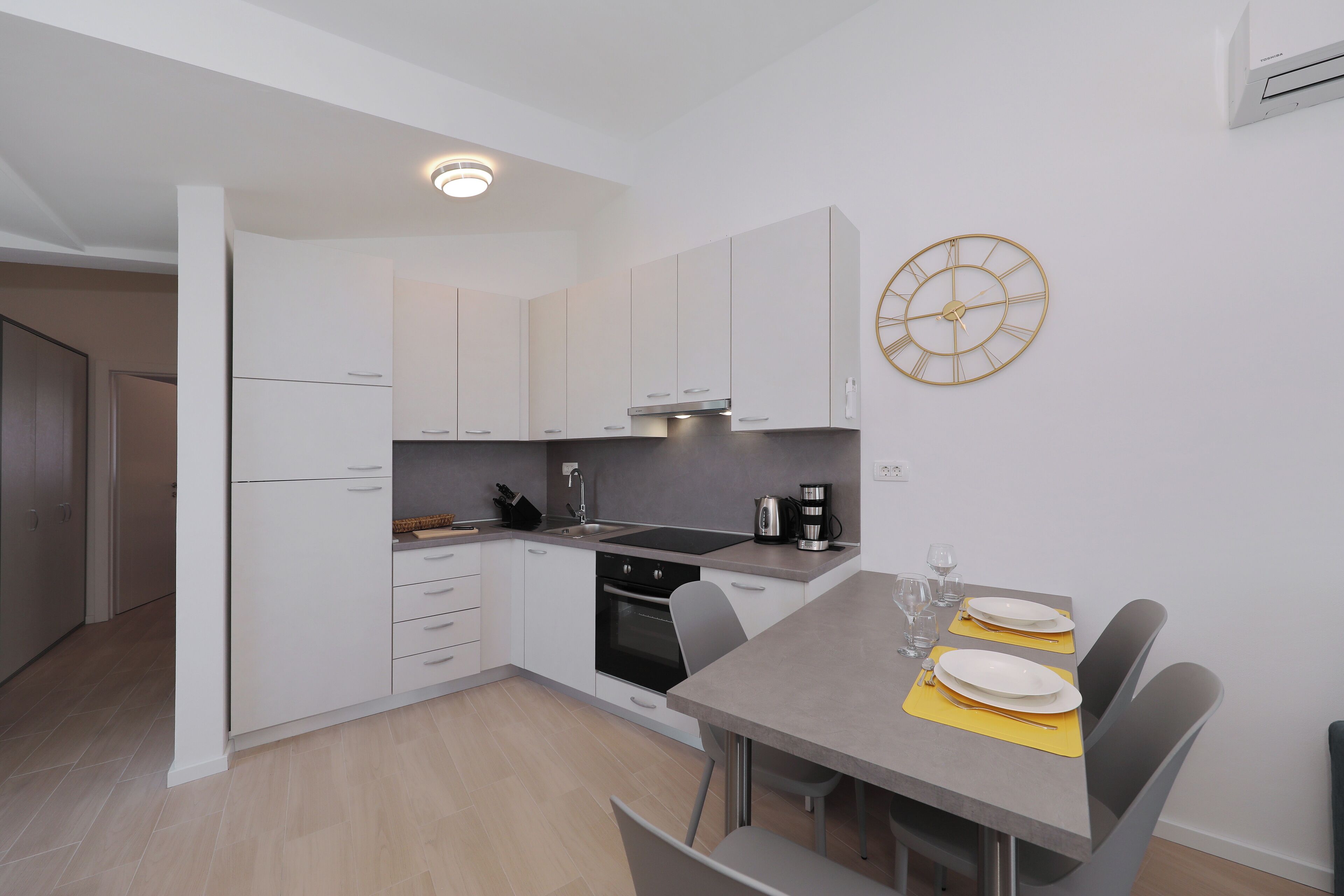 Une cuisine moderne avec des armoires blanches, un four encastré et un coin repas avec une table mise pour deux personnes.