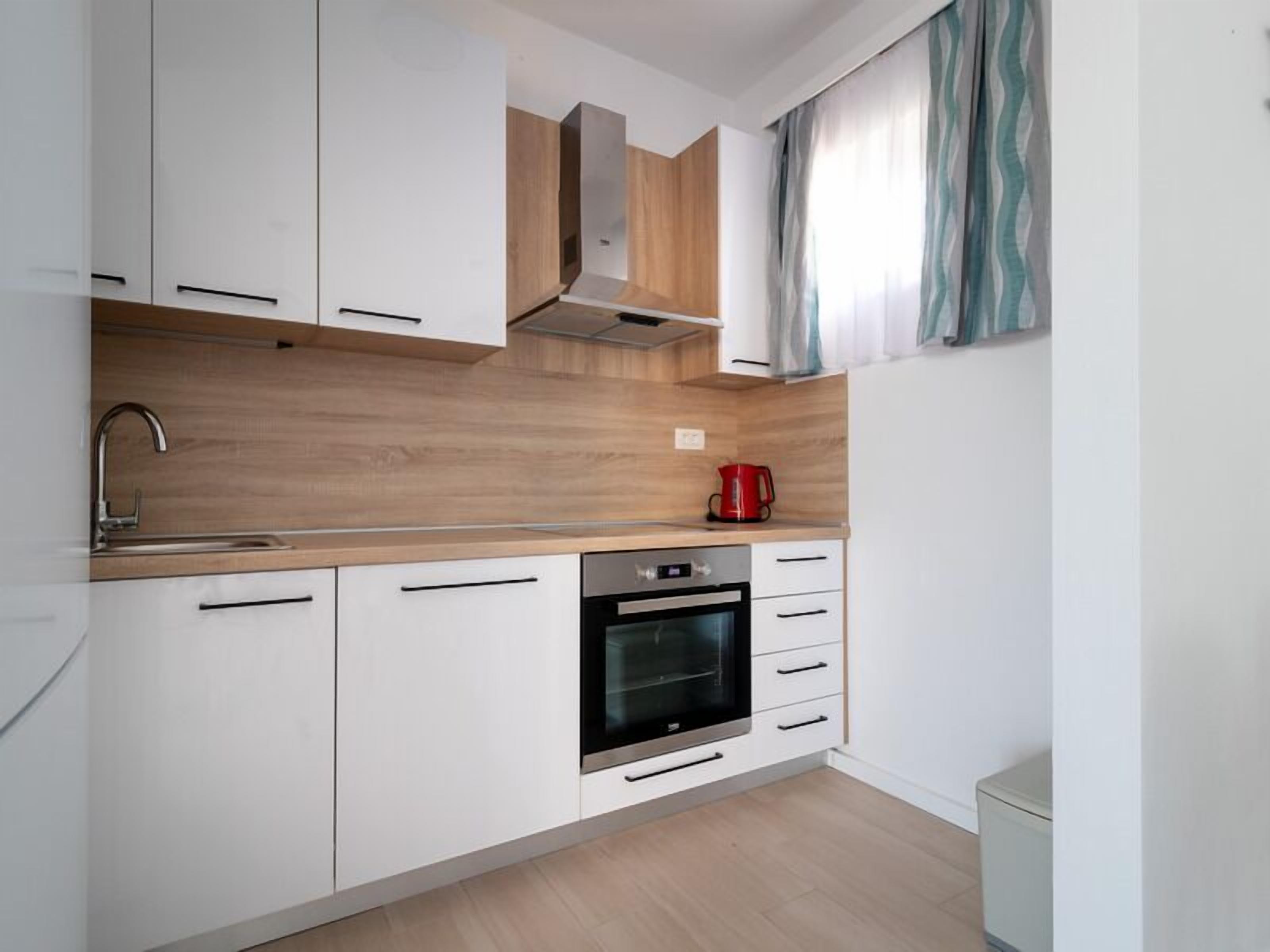 Una cocina moderna con armarios blancos, horno de acero inoxidable y encimera de madera.