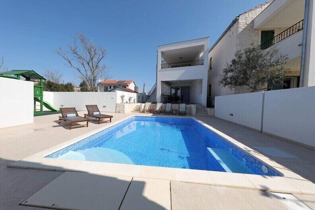 Ein moderner Poolbereich mit einem rechteckigen Pool, Liegestühlen und einem zweistöckigen Gebäude mit Balkonen.