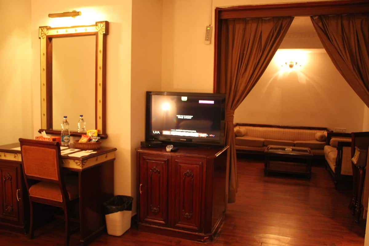 A hotel room with a wooden desk, a television, a sofa, and a large mirror.