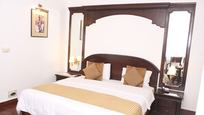 A neatly made bed with a wooden headboard, a bedside table with a lamp, and a large mirror on the wall. - Hotel J's Inn (New Delhi)