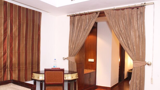A room with a wooden floor, a dining table with chairs, a sofa, and a cabinet. - Hotel J's Inn (New Delhi)