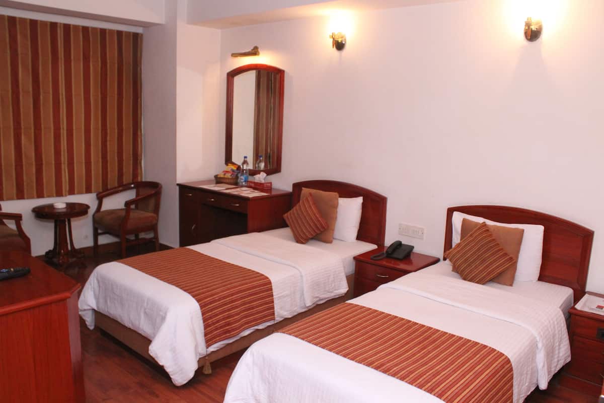 A hotel room with two beds, a desk, a chair, a nightstand, a lamp, a mirror, and a window with curtains.