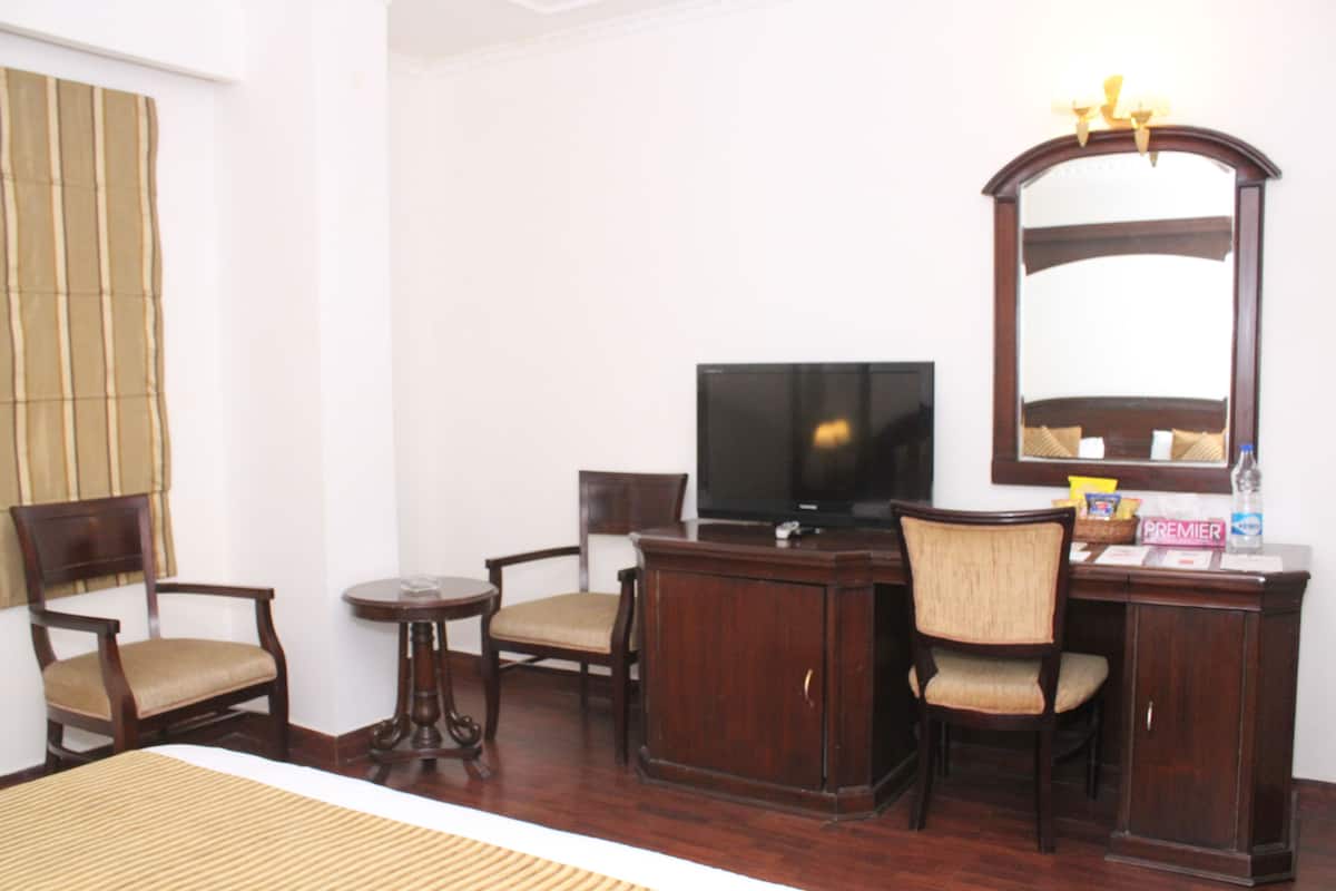 A hotel room with a bed, a TV, a desk, two chairs, a small table, and a mirror.