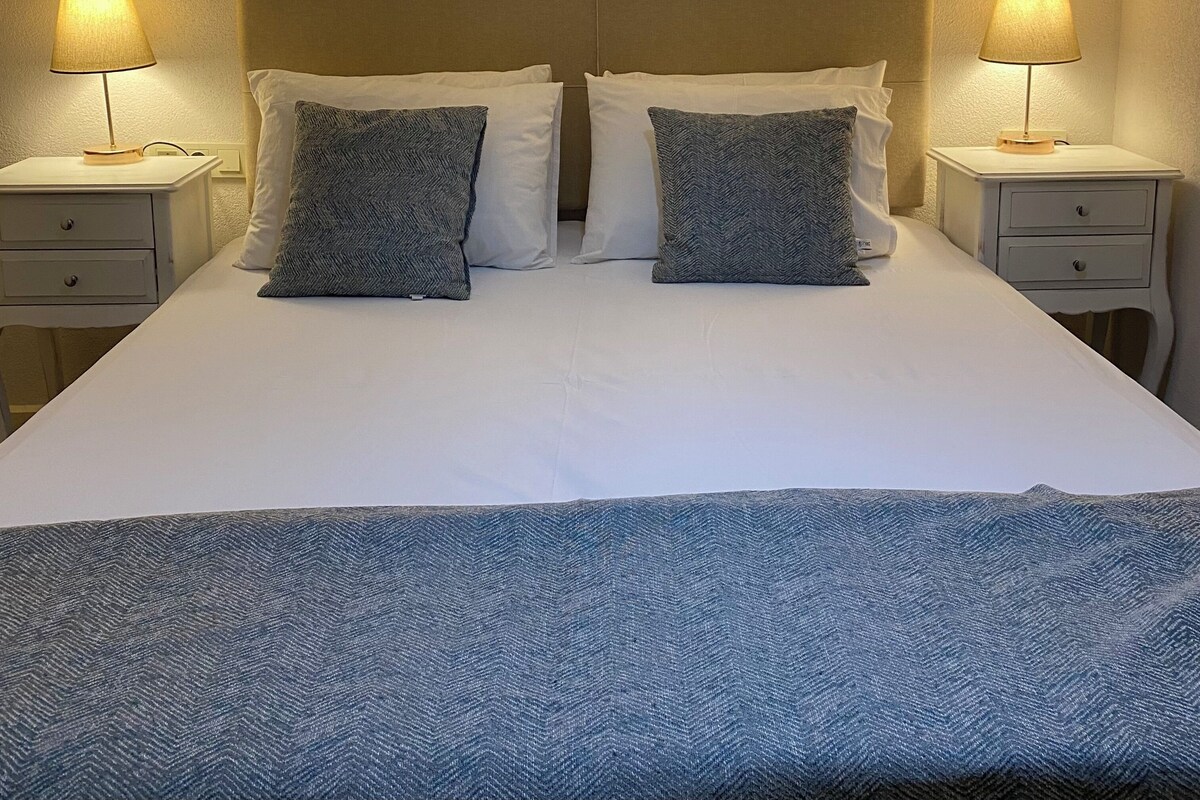 A neatly made bed with two pillows, a headboard, and two bedside tables with lamps.