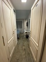 Un pasillo estrecho con puertas de madera, una cama con una colcha azul, una mesita y un televisor montado en la pared.