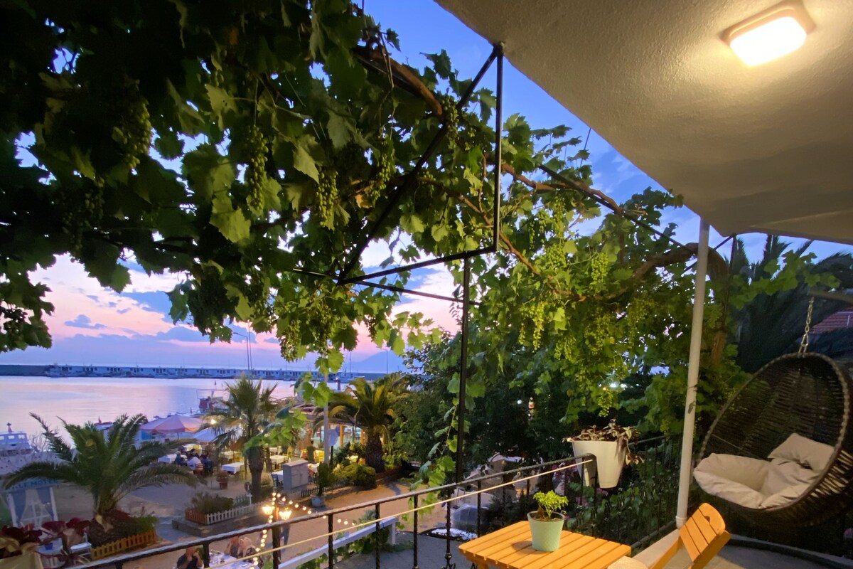 A balcony with a wooden table and chairs, overlooking a waterfront with a bridge.