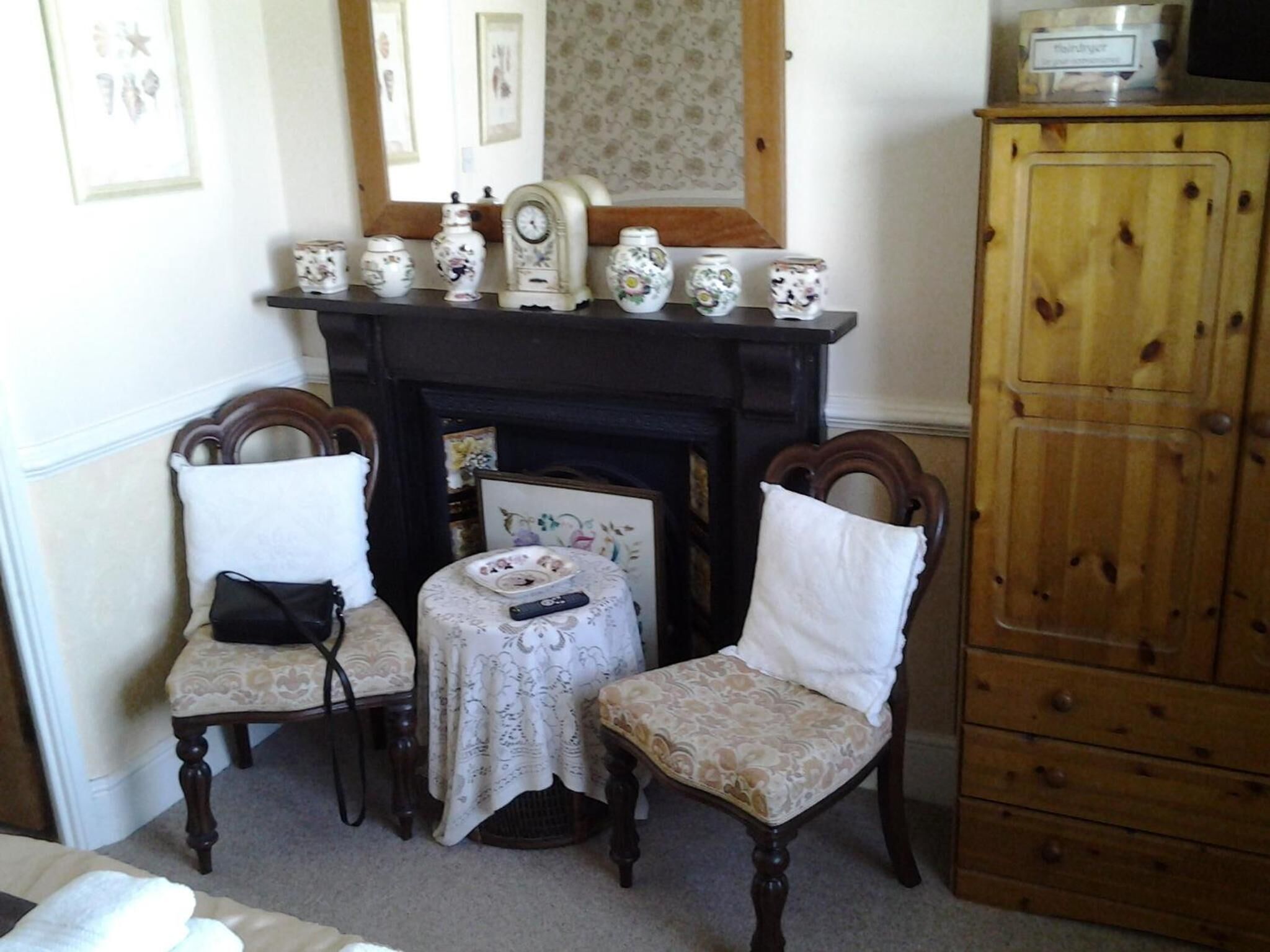A room with a fireplace, two chairs, a small table, and a wooden cabinet.