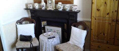 A room with a fireplace, two chairs, a small table, and a wooden cabinet.